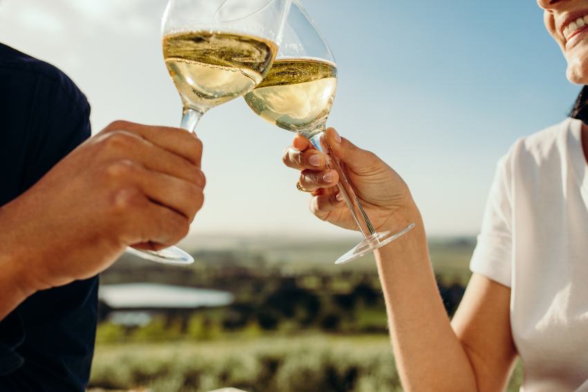 zwei Menschen prosten sich mit einem Glas Weißwein zu